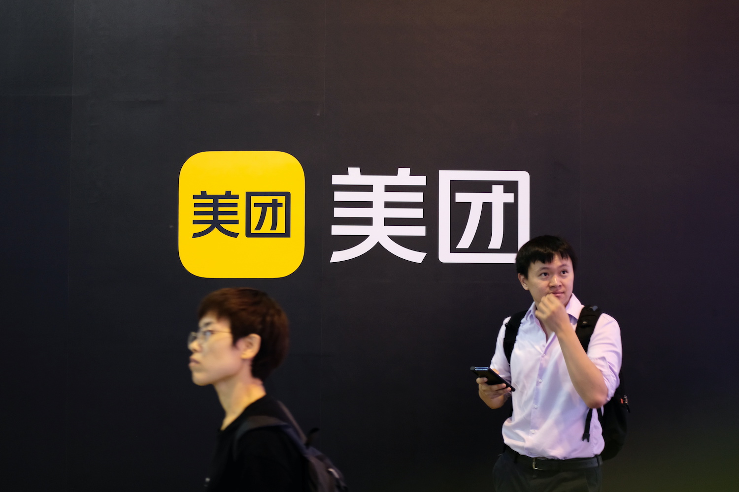 People-walk-past-a-Meituan-logo-at-the-World-Artificial-Intelligence-Conference-in-Shanghai-July-8-2021.-RtrsYilei-Sun.jpg